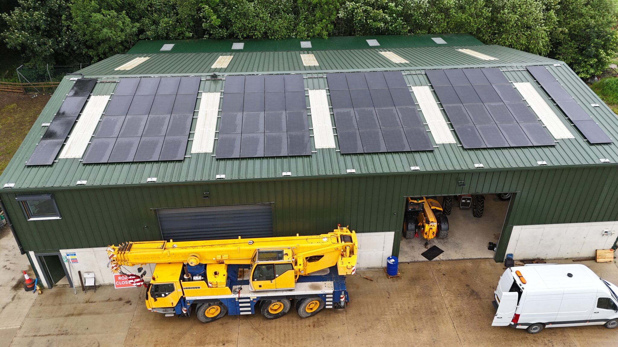 Aerial view of Park Hill Farm — the working fabrication and plant yard, with the rooftop solar array that powers the site, and a mobile crane, telehandler and van in the yard below